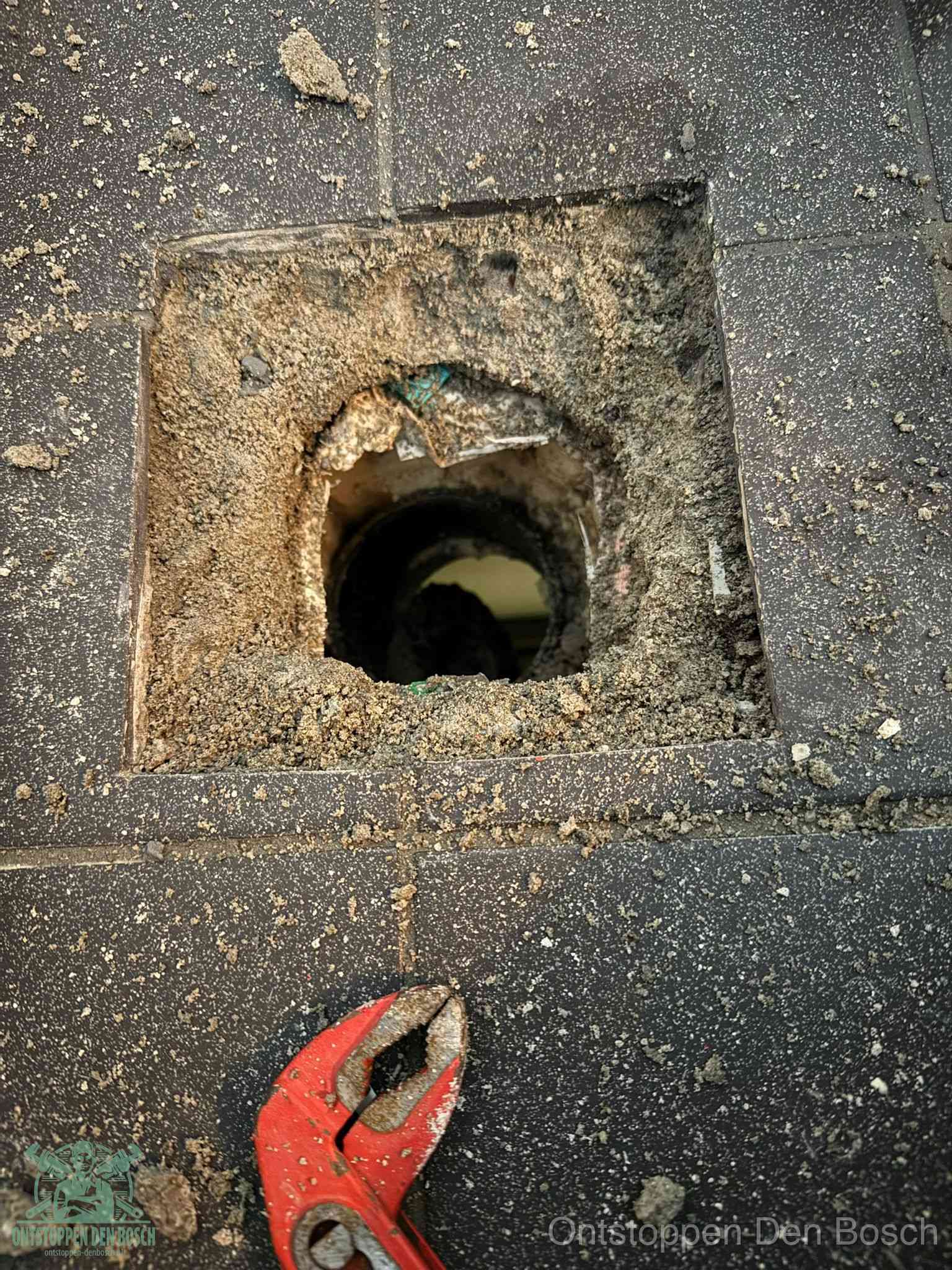 Een geopend rioolputje in een betontegelvloer met losgemaakt rooster en een zichtbare ronde afvoerbuis, het achterhalen waar de afvoerverstopping zit in Den Bosch