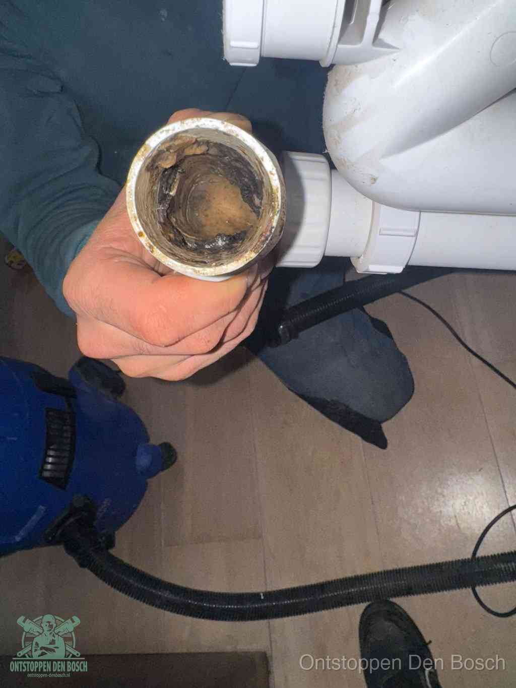 Een hand houdt een losgekoppeld PVC-afvoerbuisstuk vast dat van binnen volledig is dichtgeslibd met vet, vuil en aanslag, de meest voorkomende oorzaak van een verstopte afvoer in Den Bosch