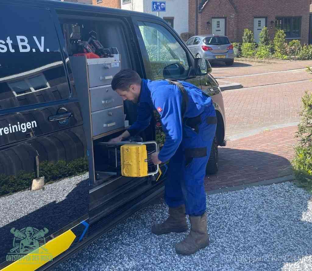 Een monteur pakt buiten op de oprit gereedschap uit de bedrijfsbus, het moment om een professional in te schakelen voor een verstopte afvoer in Den Bosch