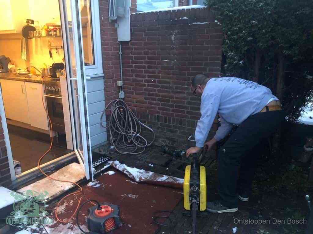 Een monteur werkt buiten bij een open riool-/grondput met een elektrische ontstoppingsmachine om een verborgen afvoerprobleem op te sporen in Den Bosch
