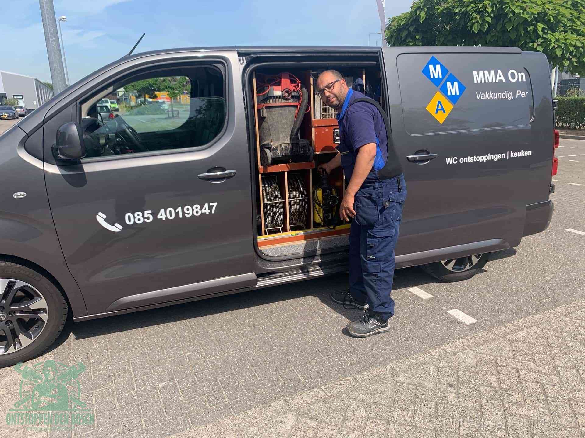 Een monteur bij de open schuifdeur van zijn bedrijfsbus op een parkeerplaats, klaar om de oorzaak van terugkerende afvoerverstoppingen aan te pakken in Den Bosch
