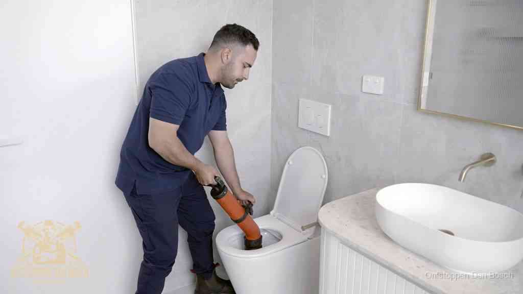 Een man gebruikt een handmatige luchtdruk-ontstopper in een modern betegeld toilet om zelf de wc te ontstoppen in Den Bosch